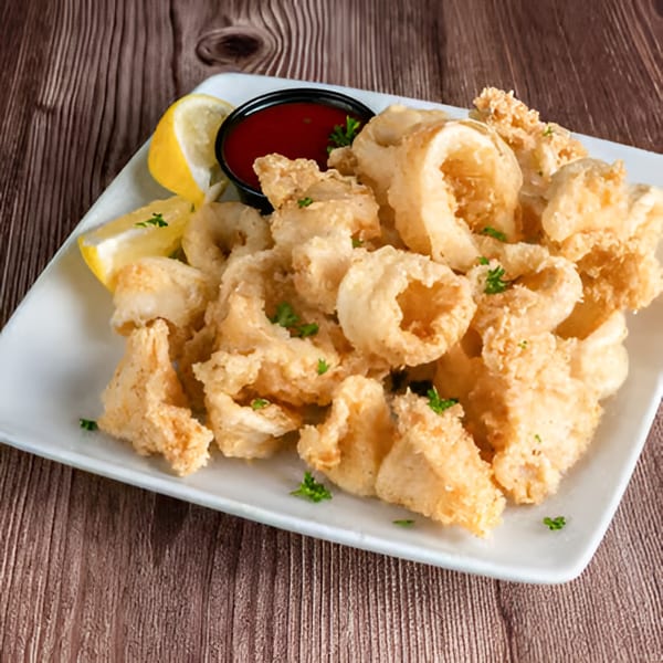 Crispy fried calamari with lemon wedges and a side of marinara sauce on a white plate.