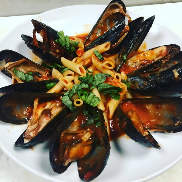 Mussels and penne pasta in red sauce, garnished with fresh basil, on a white plate.