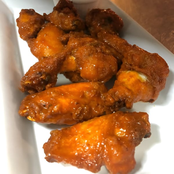Mike's Pizzeria & Italian Restaurant's buffalo wings, coated in a glistening orange sauce, on a white plate.