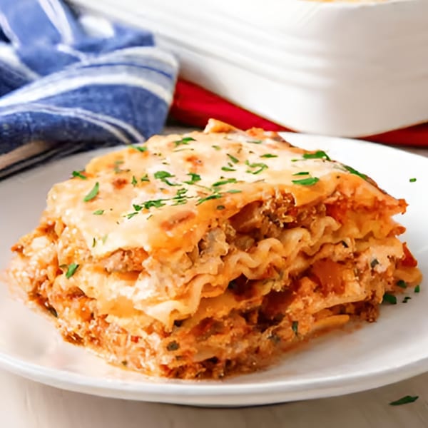 A delicious slice of Mike's Pizzeria & Italian Restaurant lasagna, topped with melted cheese and parsley.
